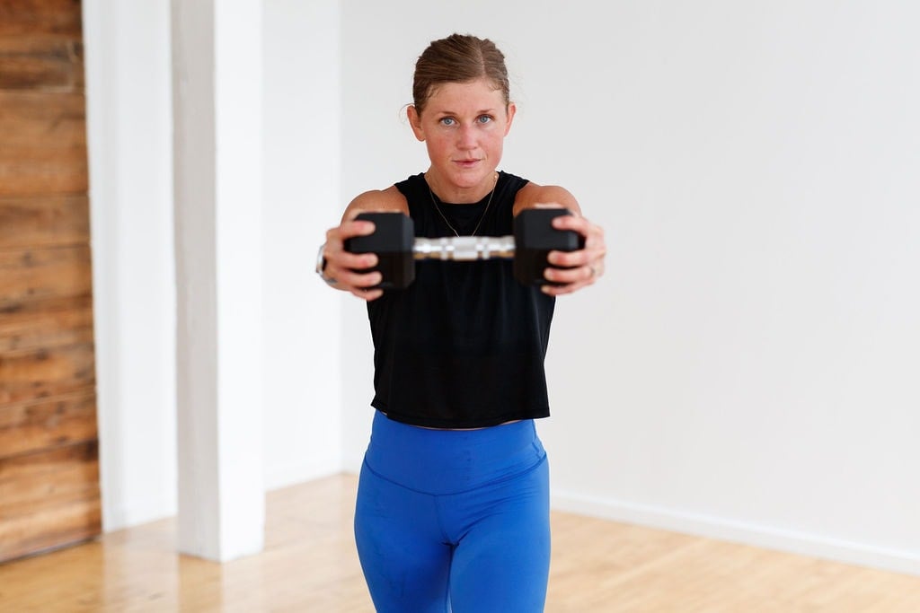 woman performing a dumbbell press out in a total body HIIT workout at home