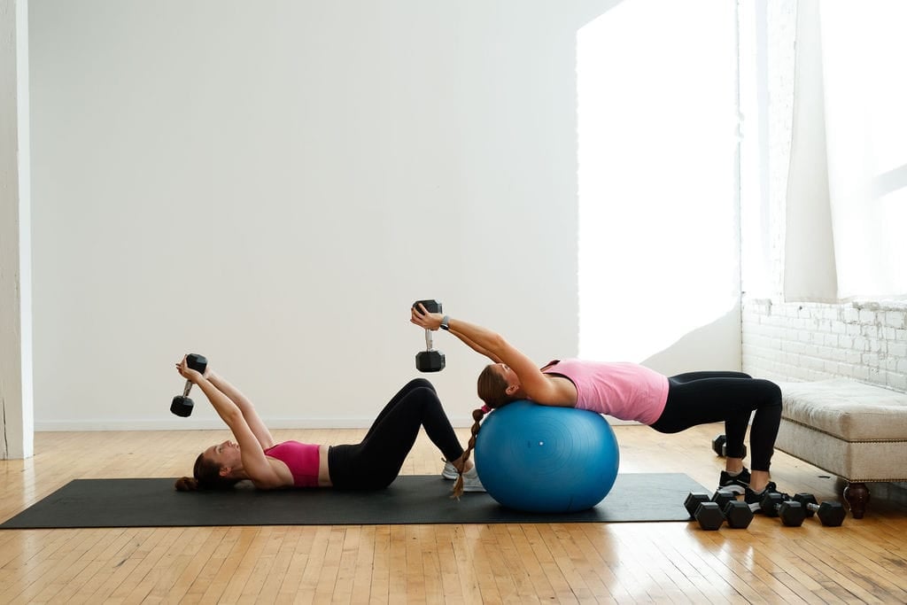 Two women performing a Dumbbell Pullover. One using a exercise ball for more back support and one laying on the ground | Arm and Back Workout