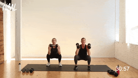 two women performing an alternating squat thruster with dumbbells