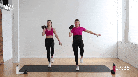 싱글 레그 밸런스 웨이트 패스;  아령을 좌우로 통과할 때 한쪽 다리로 균형을 잡는 두 명의 여성 - 서 있는 복근 운동