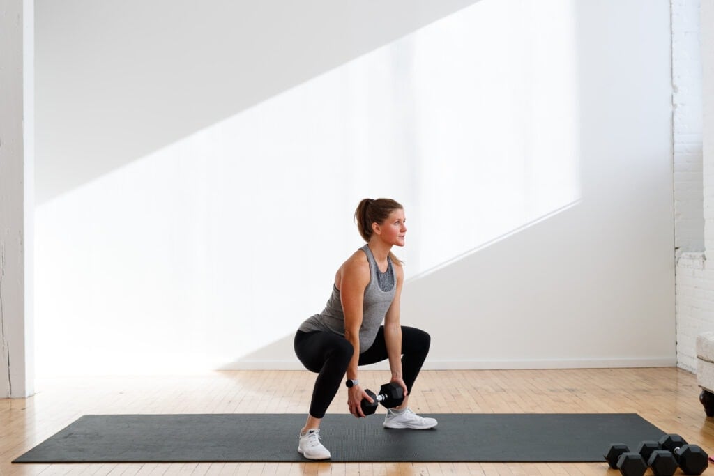 woman performing wide stance squat or sumo squat with one heavy dumbbell, best lower body exercises 