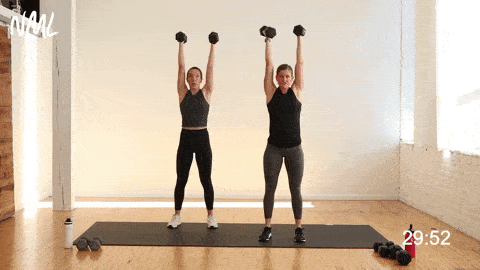 two women performing a push press shoulder exercise with dumbbells