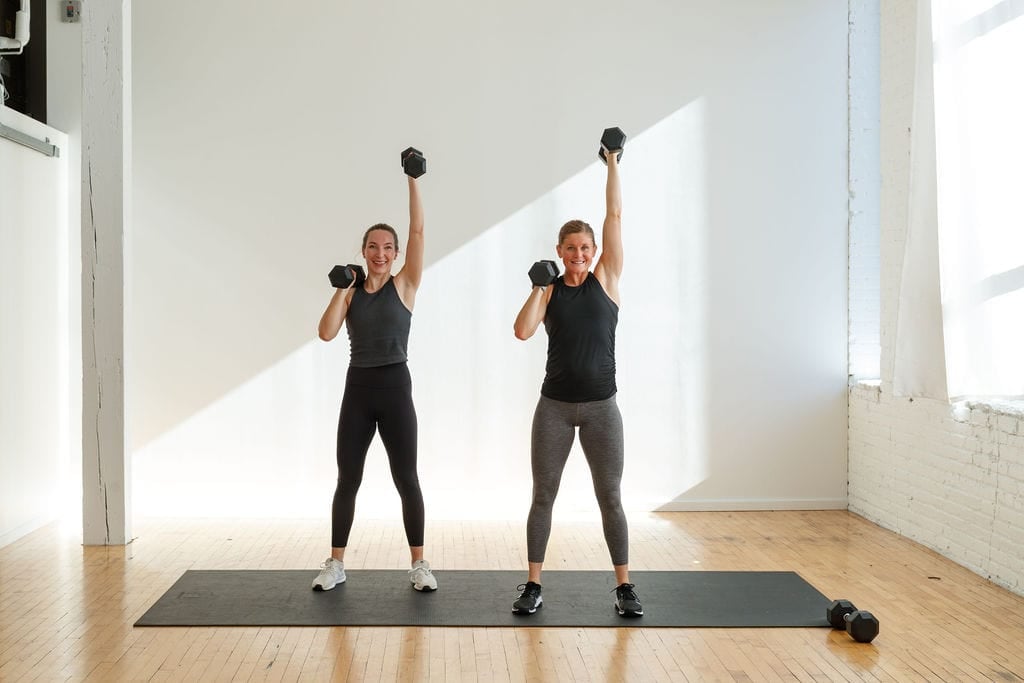 Leg and Shoulder Workout - Alternating Squat Thruster Exercise. Two women holding dumbbells performing a dumbbell alternating thruster exercise.