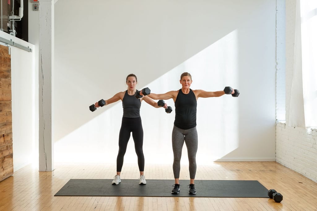 Leg and Shoulder Workout - Lateral Lunge Exercise. Two women holding dumbbells performing a dumbbell lateral raise exercise.