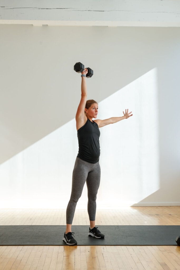 Woman performing a single arm overhead press in a Legs and Shoulders EMOM Workout