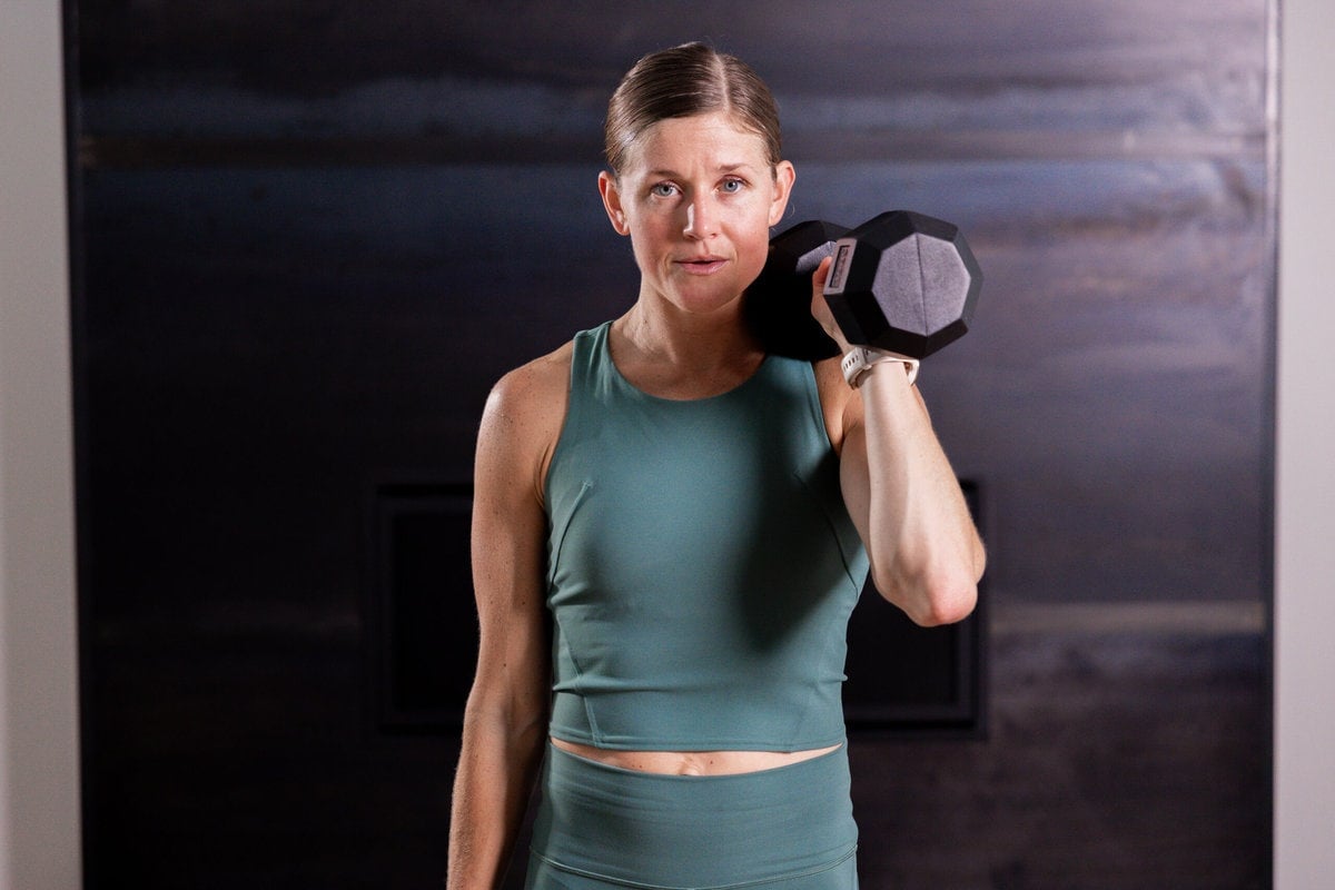 woman holding an uneven front rack with a dumbbell in a metabolic conditioning workout