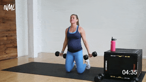 pregnant woman performing bicep curls from a kneeling position. 