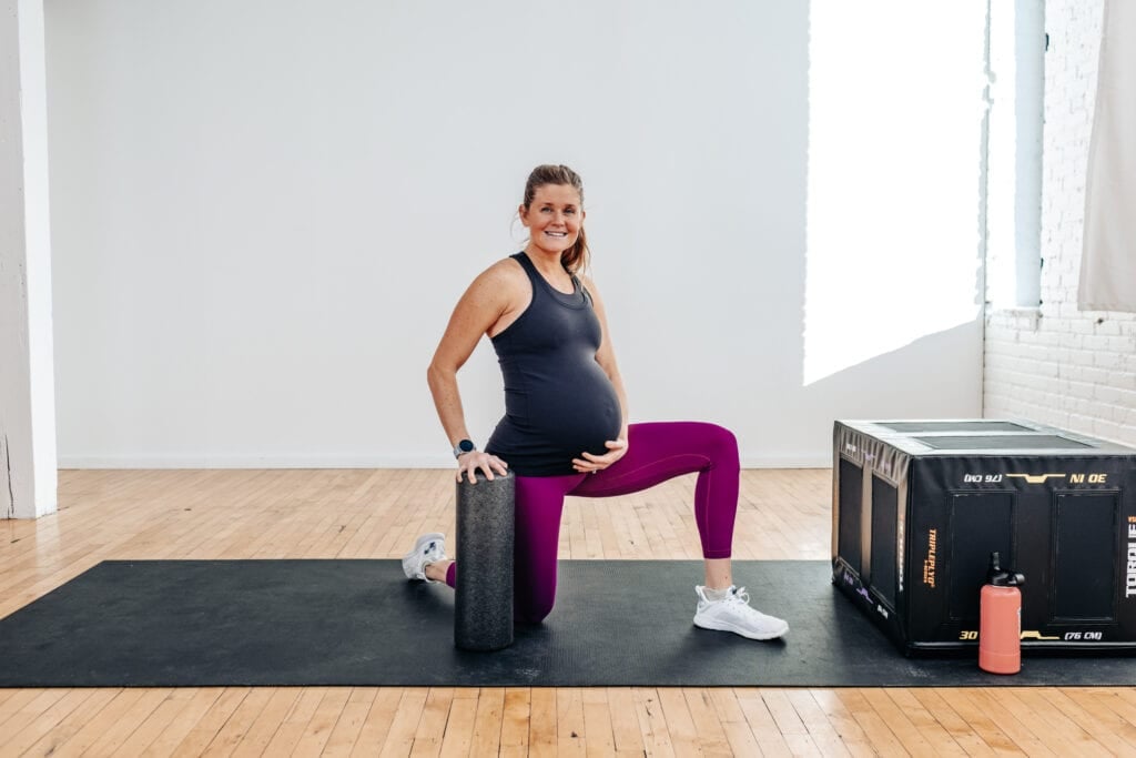 pregnant woman holding foam roller performing a hip opener stretch for back pain