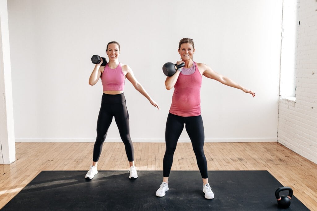 two women holding front racked kettlebell and dumbbell at shoulder height 