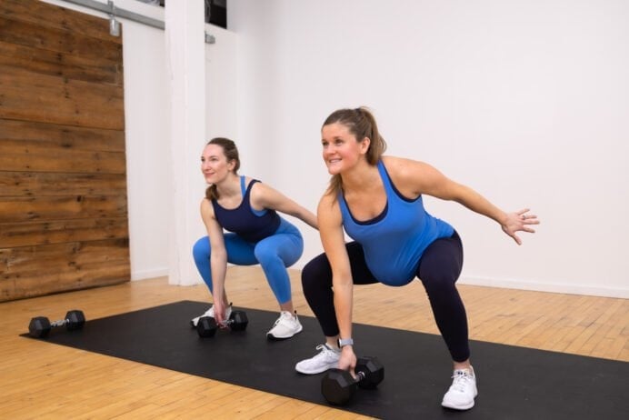 two women (one pregnant) performing a low squat dumbbell pick up