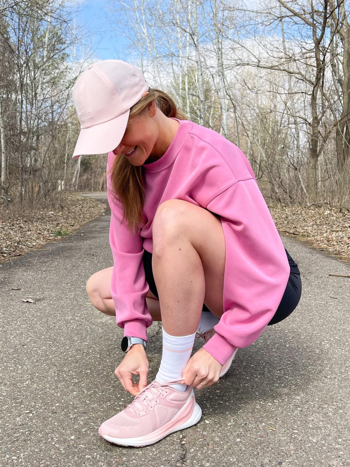 woman bending down to tie her shoes on a trail in the woods