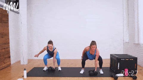two women performing a squat and snatch. One woman is pregnant and demonstrating exercise as part of a pregnancy workout at home. 