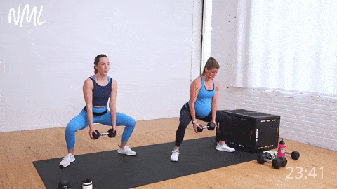 two women (one pregnant woman) performing a sumo squat and front raise