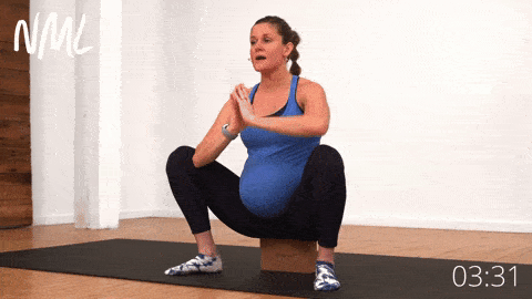 pregnant woman performing a supported wide squat hold and chest expansion on a yoga block in prenatal yoga routine