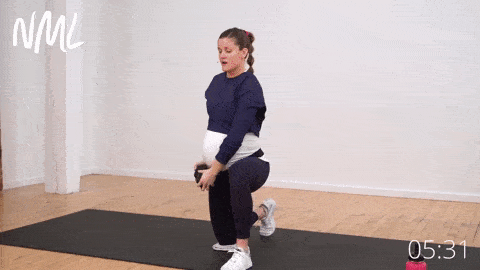 pregnant woman kneeling and performing cross body chop with a single dumbbell