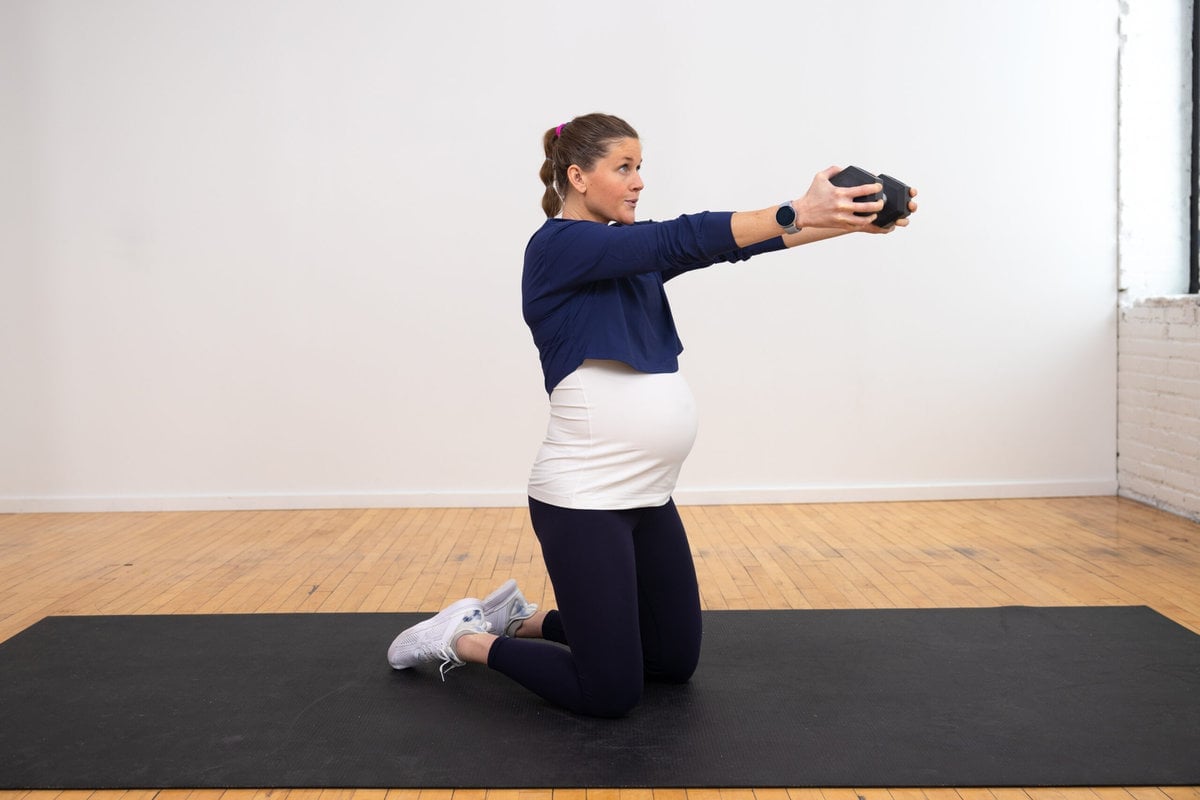pregnant woman performing a kneeling front raise with a dumbbell as part of prenatal core workout