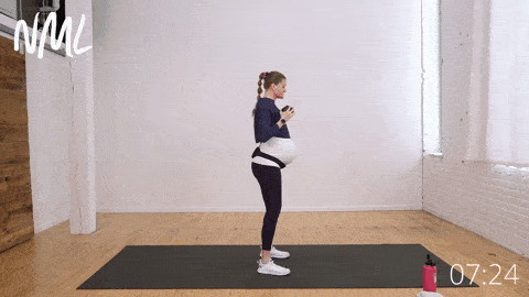 pregnant woman standing and performing a dumbbell press out with deep belly breathing