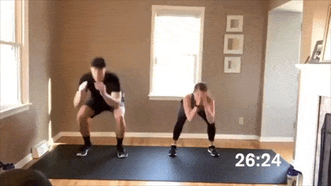 man and woman performing squat jumps in a HIIT workout at home