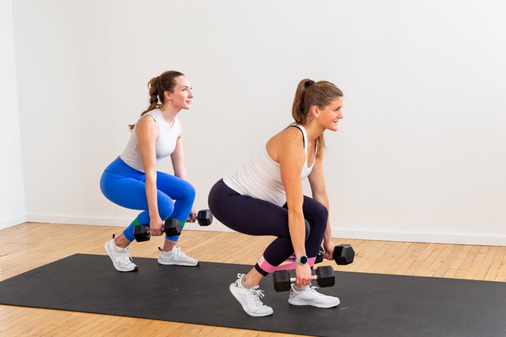 two women performing a staggered squat with dumbbells