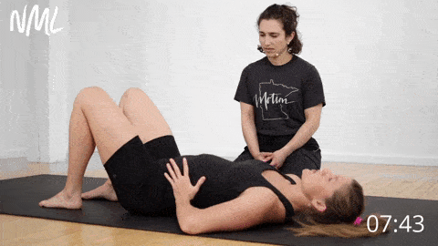postpartum woman wearing all black lying on yoga mat performing alternating heel slides with a leg lift to strengthen postpartum abs