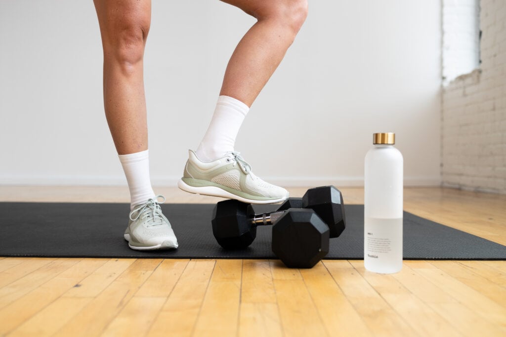 close up image of cross training shoes with weights and water bottle