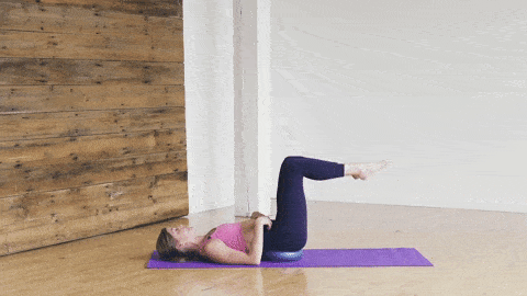 woman performing alternating lying bent knee toe taps with pilates ball under low back to engage core