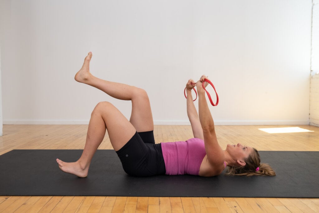 postpartum woman performing heel taps with resistance band pull apart