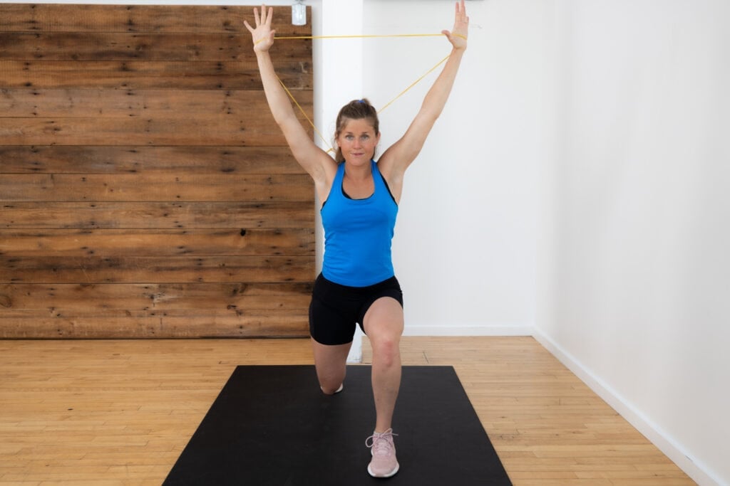 postpartum woman pulling resistance band overhead as part of postpartum ab workout