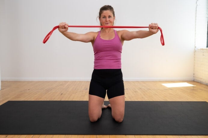 Postpartum woman performing a resistance band pull apart to rebuild core strength after babies