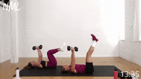 two women lying on their backs performing skull crushers and leg lowers as part of total body dumbbell workout