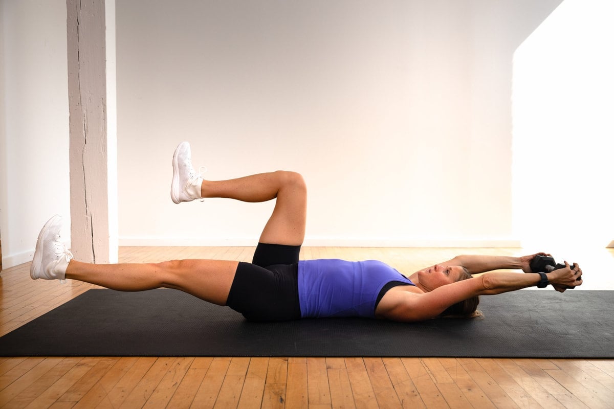 woman lying on her back performing a dead bug with weights