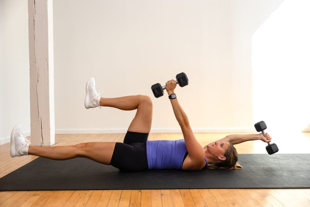 woman lying on her back performing a weighted dead bug exercise