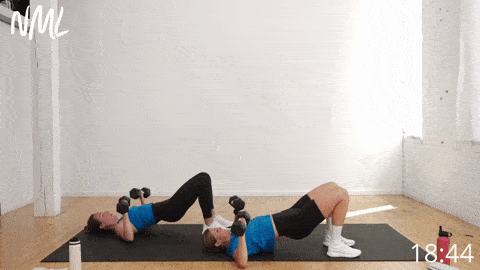 two women lying on a black mat performing a glute bridge chest press example of strength training exercises