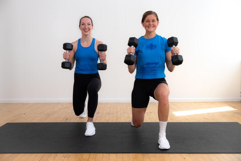 two women performing a reverse lunge with dumbbells front racked as part of strength training workout for women