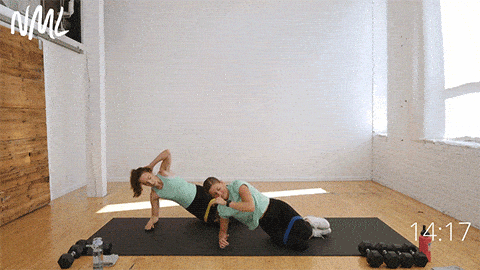 Two women lying on a black mat performing a clamshell exercise as part of abs and glutes workout