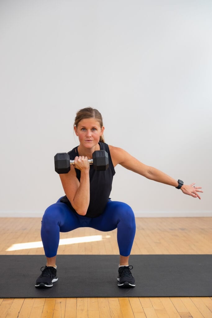woman holding a low squat with dumbbell front racked as part of leg and back workout