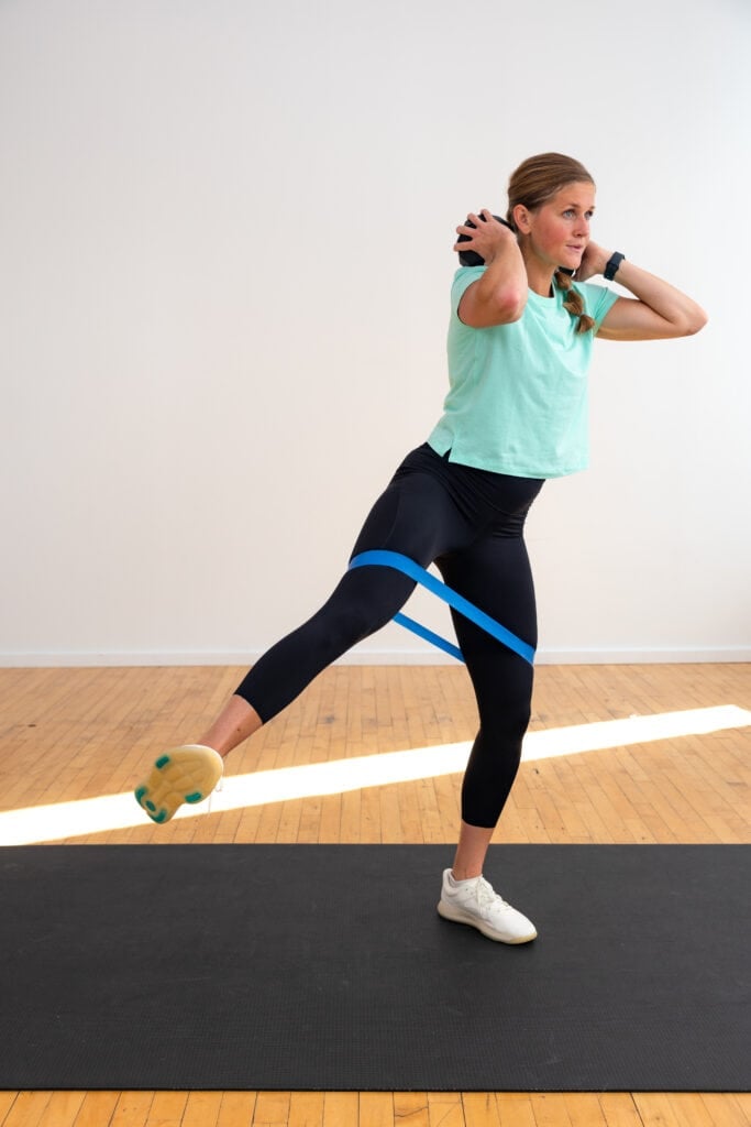 woman performing a squat and leg lift with mini loop resistance band around her thighs