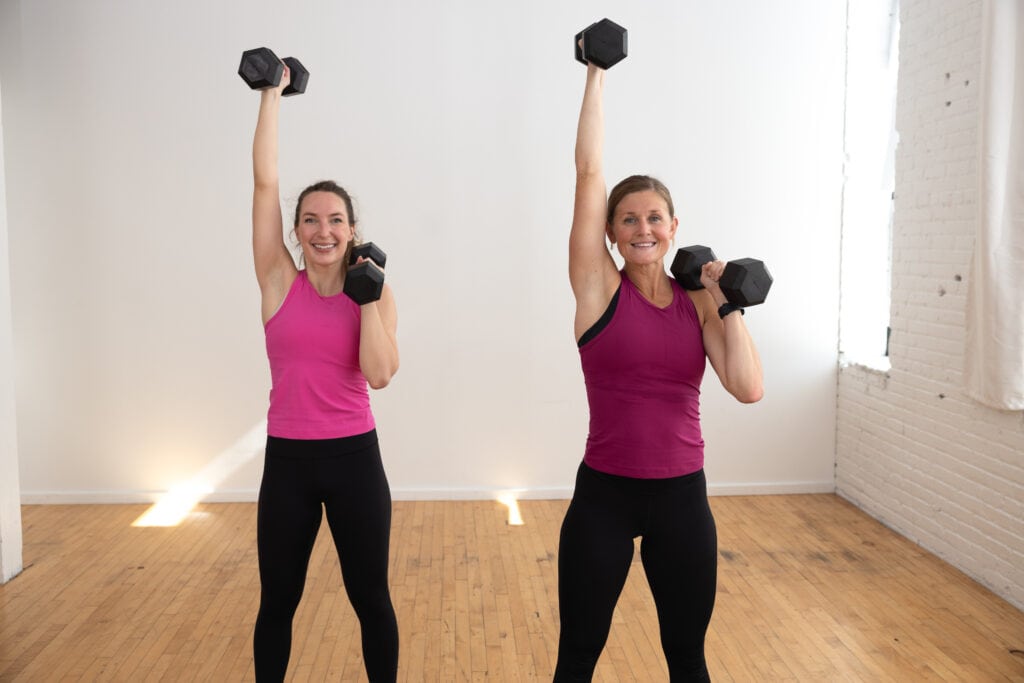 two women performing a single arm overhead shoulder press with dumbbells in a functional strength workout