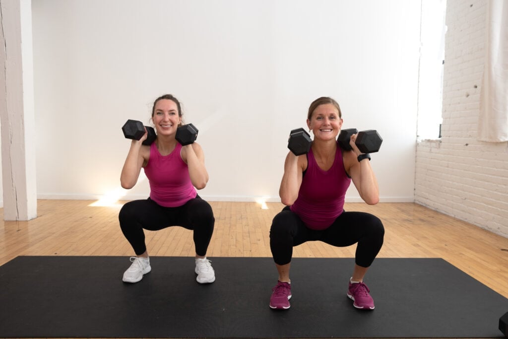 two women performing a dumbbell squat with dumbbells front racked
