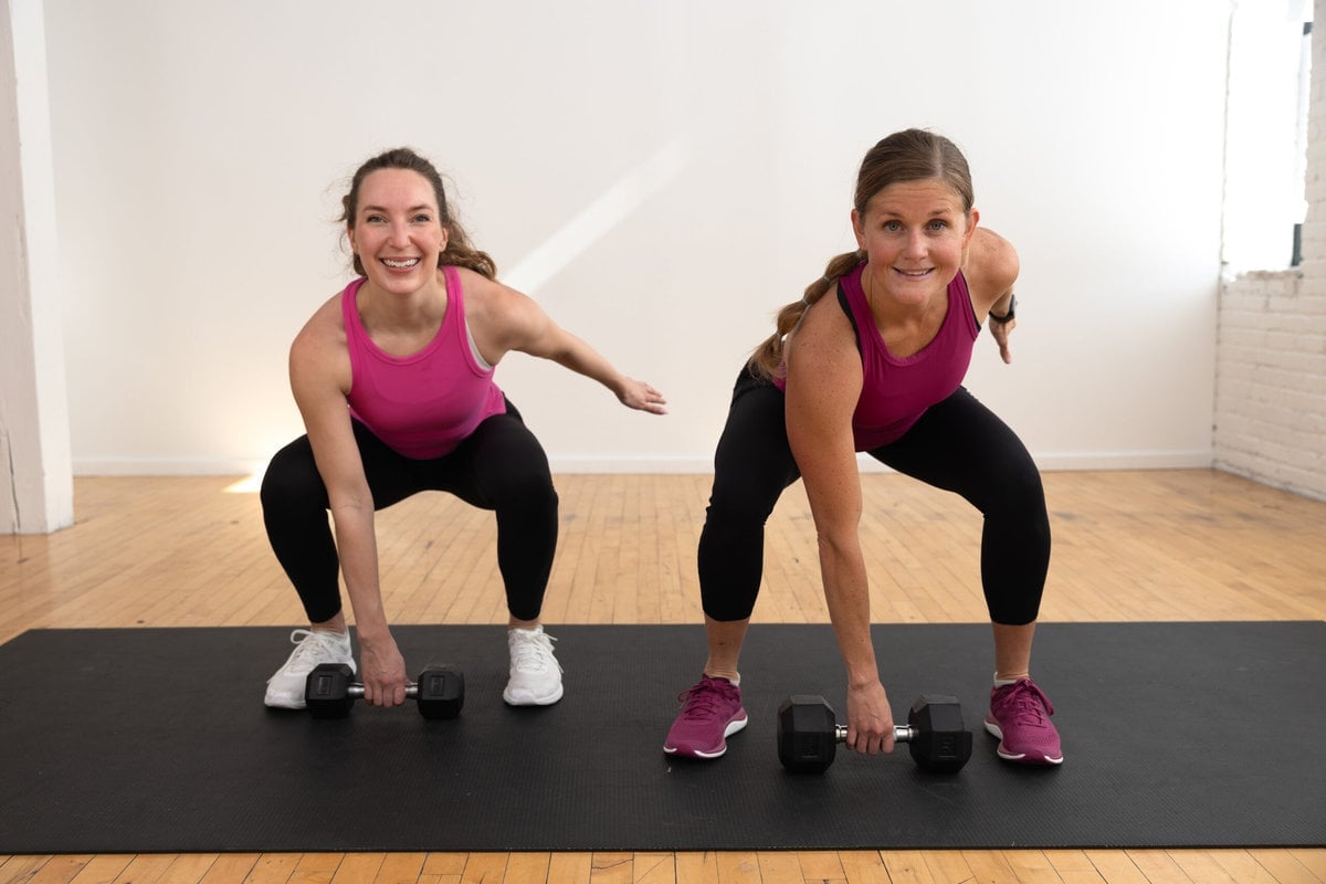 two women performing a squat hold preparing to do a dumbbell overhead snatch in a full body workout