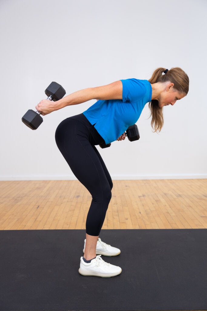 woman standing performing a single arm tricep kickback as part of back and arm workout