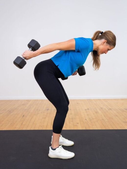 woman standing performing a single arm tricep kickback as part of back and arm workout
