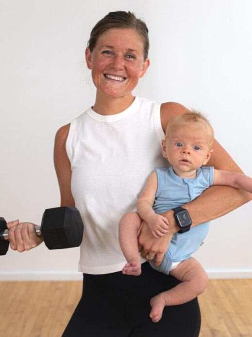 postpartum woman holding a baby and a dumbbell