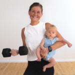 postpartum woman holding a baby and a dumbbell. For postpartum workouts plan.