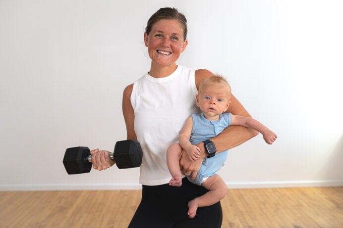 postpartum woman holding a baby and a dumbbell. For postpartum workouts plan.