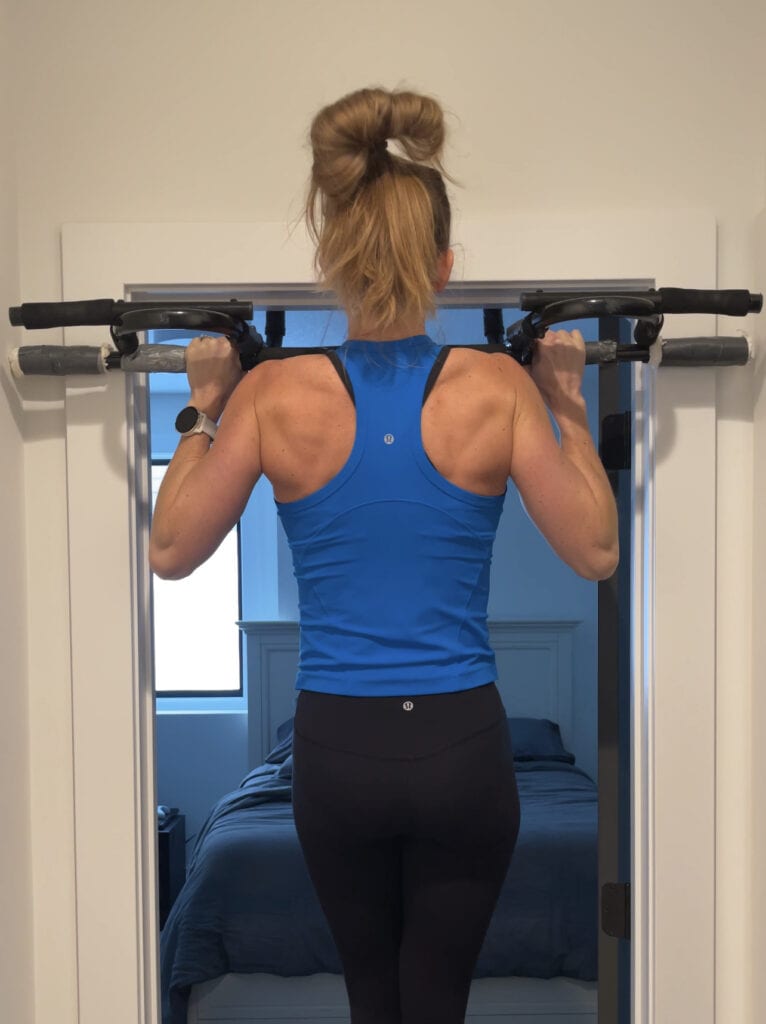 Woman performing a pull up on a multiple grip pull up bar from Amazon. The pull up bar is one of the best pieces of exercise equipment for at home fitness.