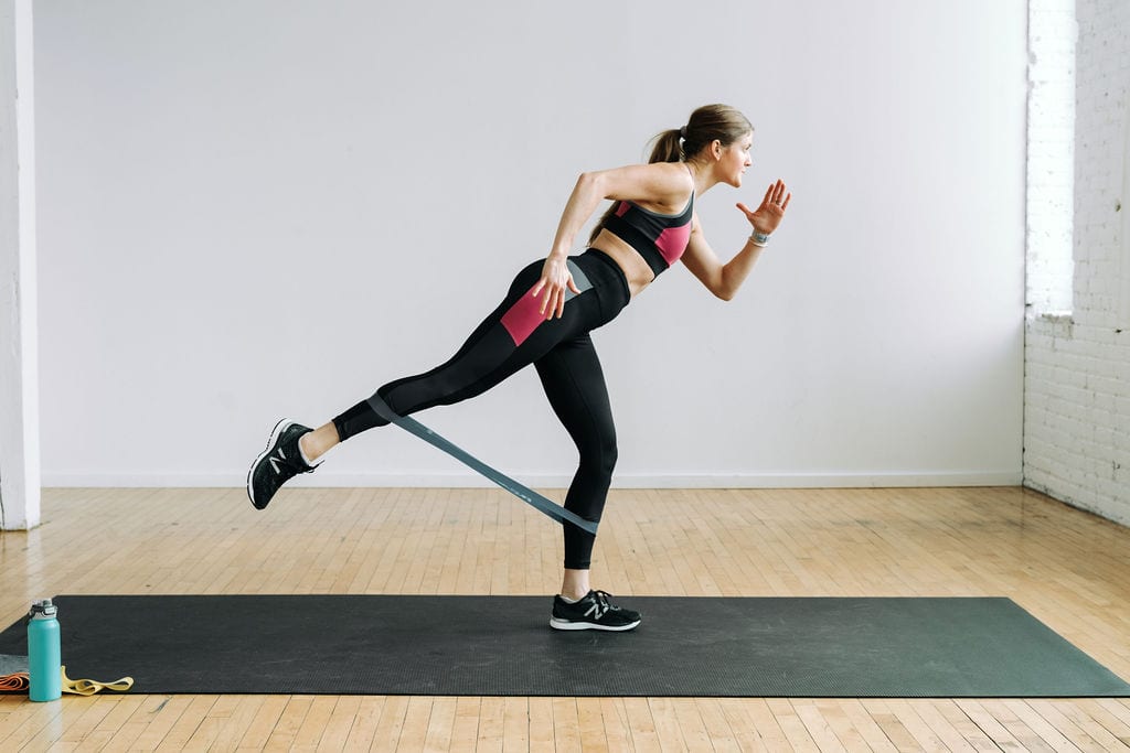 Women performing a staggered squat and leg lift in a resistance band leg workout. 