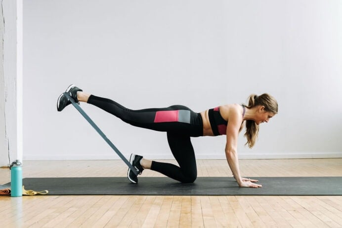 Women performing a table top single leg kick back and lift workout, during a resistance bands leg workout.