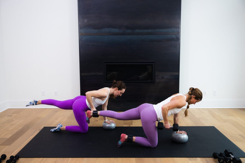 two women performing a quadruped bird dog and single arm row in a pilates workout