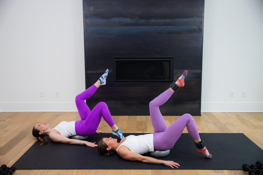 two women performing a single leg glute bridge with a pilates ball in a pilates strength workout